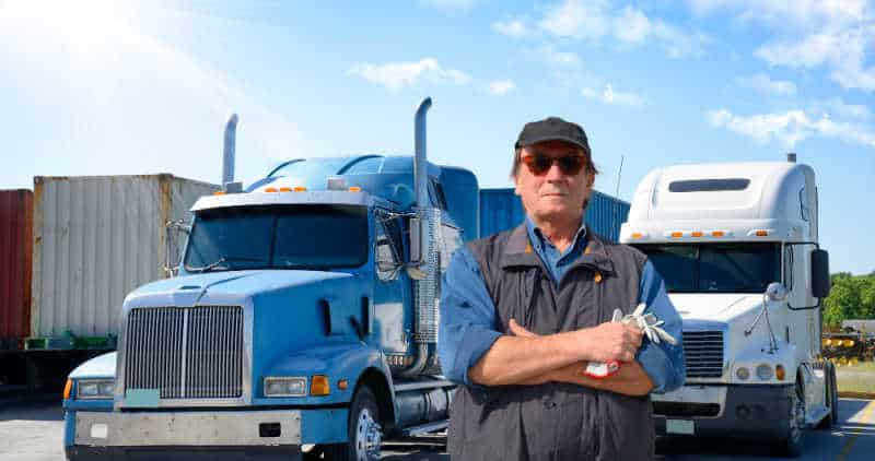 https://www.smart-trucking.com/wp-content/uploads/2021/01/Older-truck-driver-in-front-of-2-trucks.jpg